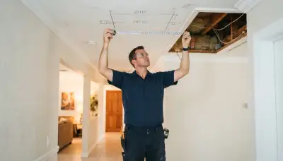 Electrician measures ceiling joist spacing for whole-house fan installation in Fort Lauderdale, FL